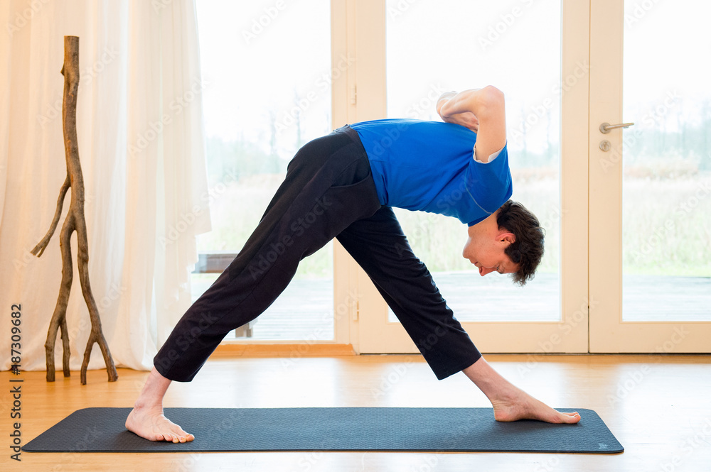 Man practicing yoga indoors in a retreat space doing Intense Side Stretch Pose - Parsvottanasana Man practicing yoga indoors in a retreat space doing Intense Side Stretch Pose - Parsvottanasana