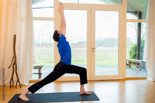 Man practicing yoga indoors in a retreat space doing Warrior 1 pose - Viradhadrasana I