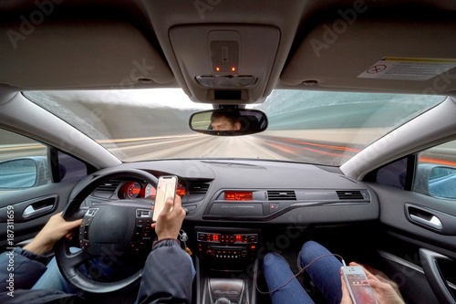 Dangerous driving while writing SMS text message. Man with momile phone in hand and young woman in a car speedy driving on highway.