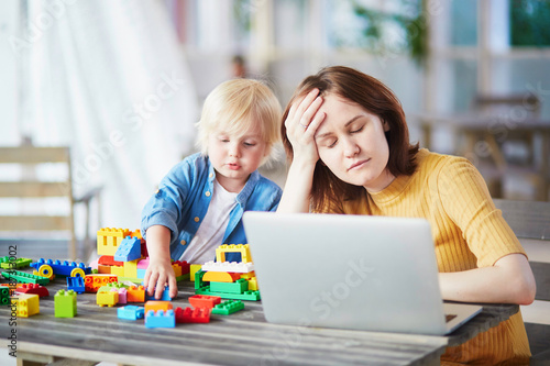 Little boy playing with construction blocks while his mother working on computer