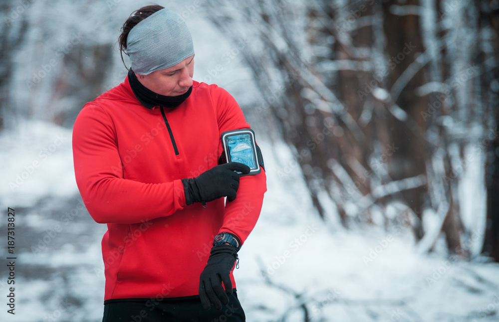 Runner using phone armband wearing warm running clothes, winter exercise outdoor Runner using phone armband wearing warm running clothes, winter exercise outdoor