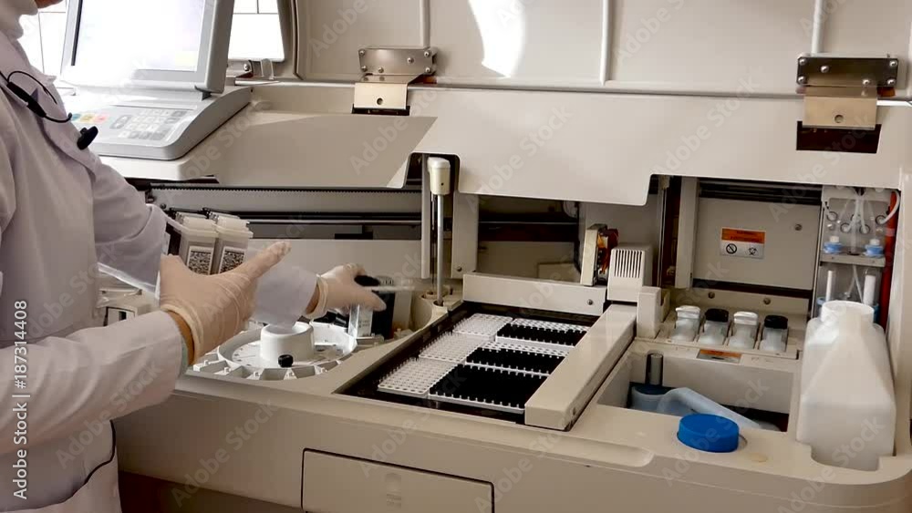 the girl in the lab puts the serum samples in a medical device for analysis. Machine automatic biochemical analysis. Indoors. The camera is fixed the girl in the lab puts the serum samples in a medical device for analysis. Machine automatic biochemical analysis. Indoors. The camera is fixed