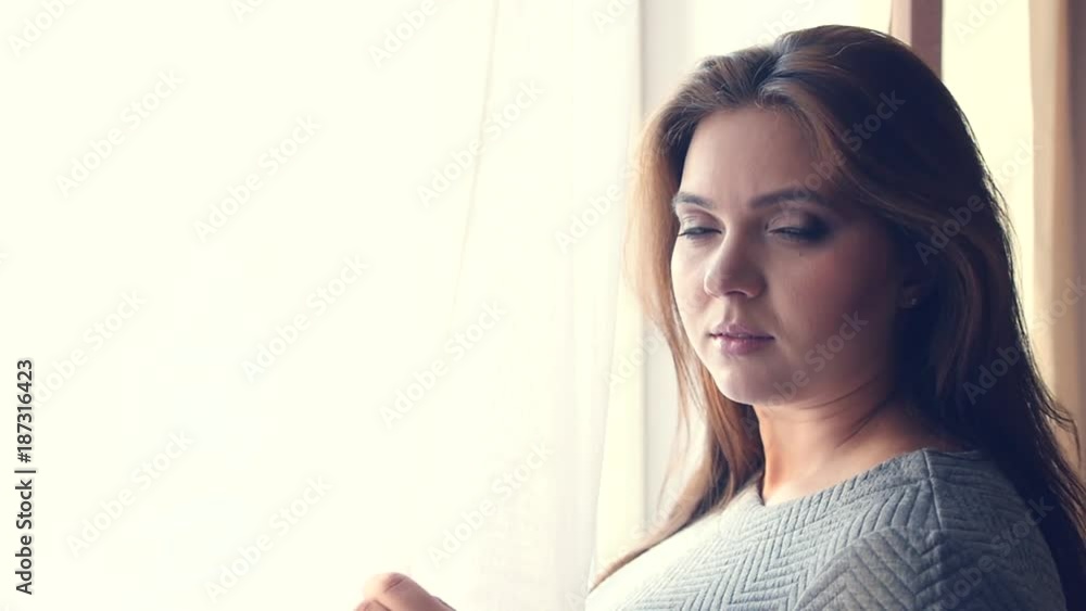 A beautiful girl stands by the window with curtains, looks into the camera and turns away. HD, 1920x1080, slow motion A beautiful girl stands by the window with curtains, looks into the camera and turns away. HD, 1920x1080, slow motion