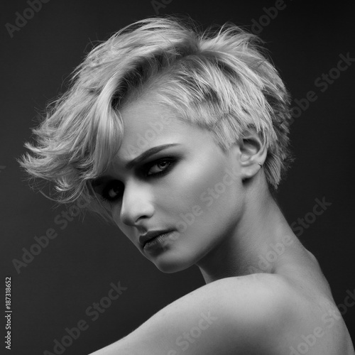 Black and white fashion beauty portrait of a blonde girl with a stylish short haircut on a gray background.