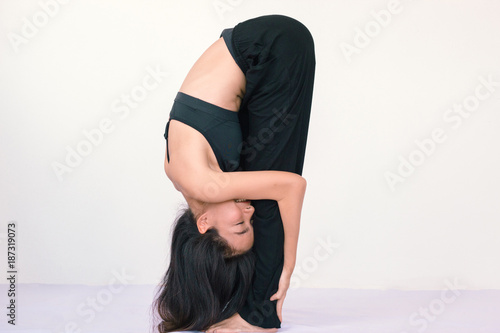 Yoga morning routine, fitness, sport and healthy lifestyle concept - young asian woman doing yoga standing forward bend pose with blank white wall copy space