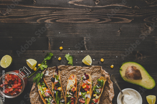 Mexican tacos with vegetables, salsa and avocado on the wooden background, top view