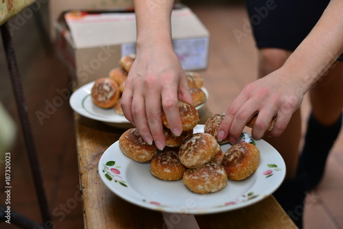 The girl at the table pours the tea into a cup. On the table lie cakes, eclairs. Traditional French dessert. Breakfast in the village. A woman is eating sweets. Against a dark background.