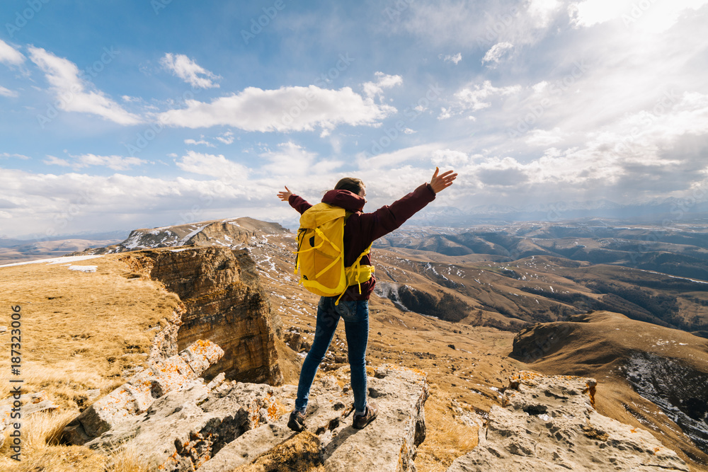 Obraz premium a young girl with arms outstretched stands on the edge of a cliff