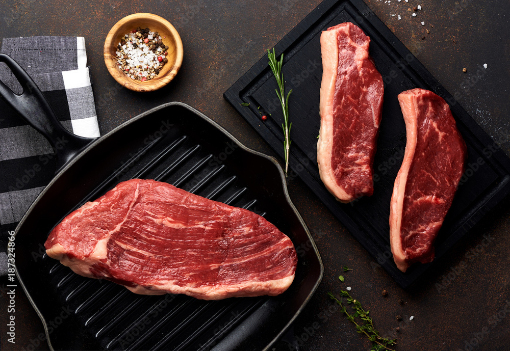 Raw fresh meat Picanha steak, traditional Brazilian cut with thyme, garlic, and black pepper on wooden board. Sliced meat Black Angus steak on grill iron pan. Top view.