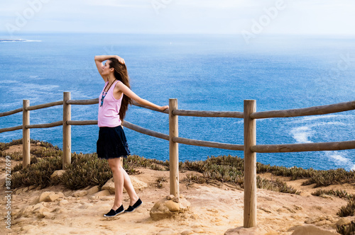 Stylish young woman standing at the very edge of the rock and staring into the distance (the place where the earth ends and the sea begins, Cabo da Roca (Cape Roca), Sintra, Portugal)
