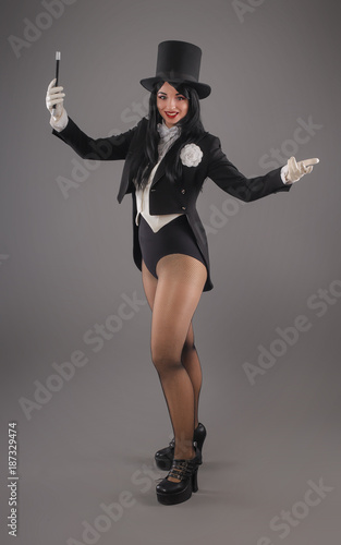 Female magician in costume suit with magic stick doing trick