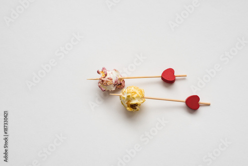 Still-life of festive multicolored popcorn on Valentine's day with colorful popcorn and two red hearts on white background