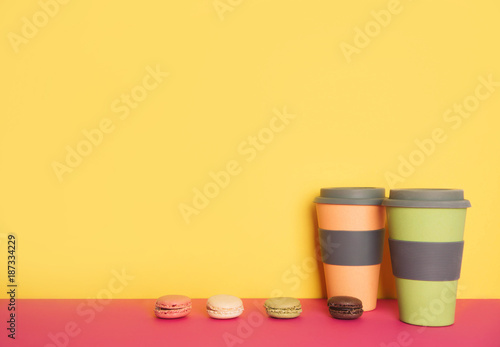 Cup of coffee to go with macaron on yellow and pink background