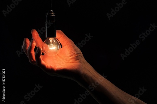 Incandescent light bulb in a hand on a black background.