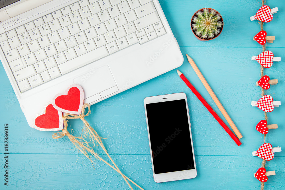 workplace on a blue laptop background, smartphone and red decorative hearts, pencils. Valentine day, holiday background