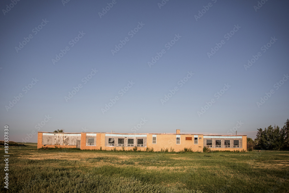 A boarded up and abandoned old brick school on a large patch of lawn in a rural landscape