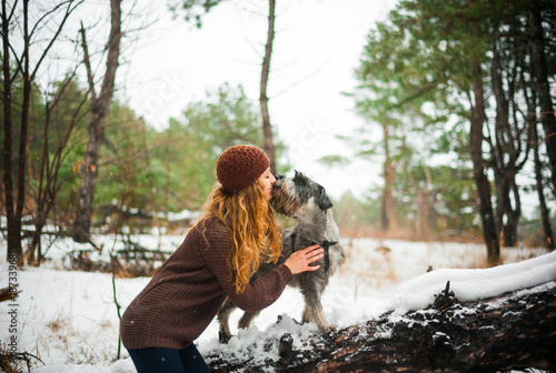 curly haired red-haired girl on a walk with a dog schnauzer in the winter afternoon in the forest