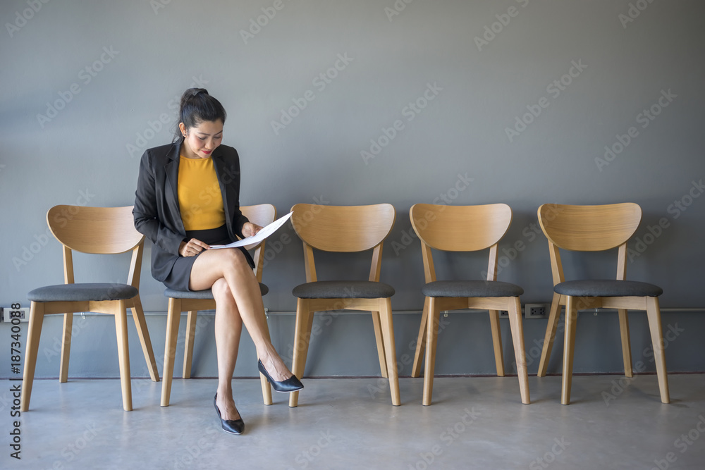 Fototapeta premium A woman sitting in a chair reading a document while waiting for a job interview in the waiting room.