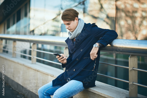 Young businessman using smart phone while standing on the street.