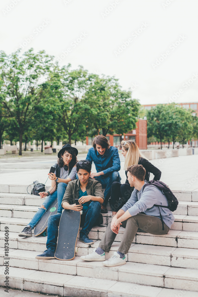 Obraz premium Group of friends multiethnic sitting outdoor using smart phone - technology, phubbing, internet concept