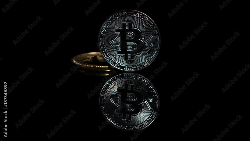 Two bitcoins reflecting on dark glass table