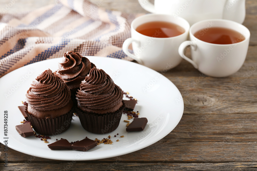 Tasty cupcakes with pieces of chocolate in plate and cup of tea on wooden table Tasty cupcakes with pieces of chocolate in plate and cup of tea on wooden table