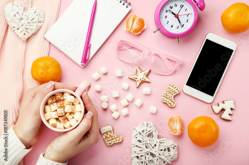 Female hands holding cup of coffee with marshmallow, mandarins and gingerbread cookies