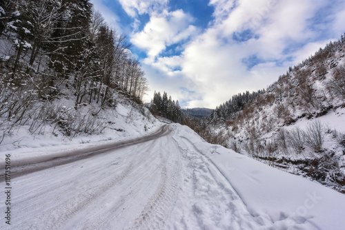 Narrow winding mountain road in snow, daytime winter landscape with blue cloudy sky