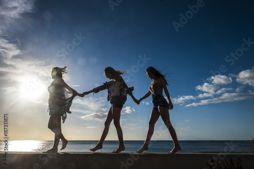 Group of three girls walking on a wall near the beach