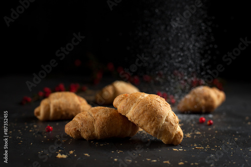 several whole croissants with crumbs and red berries on a dark background