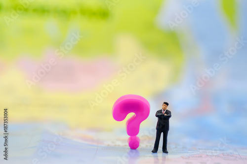 Global Business and Planning Concept. Businessman miniature figure standing on world map with pink question mark symbol plastic toy.