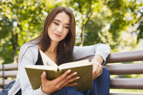 Young woman reading book in park copy space