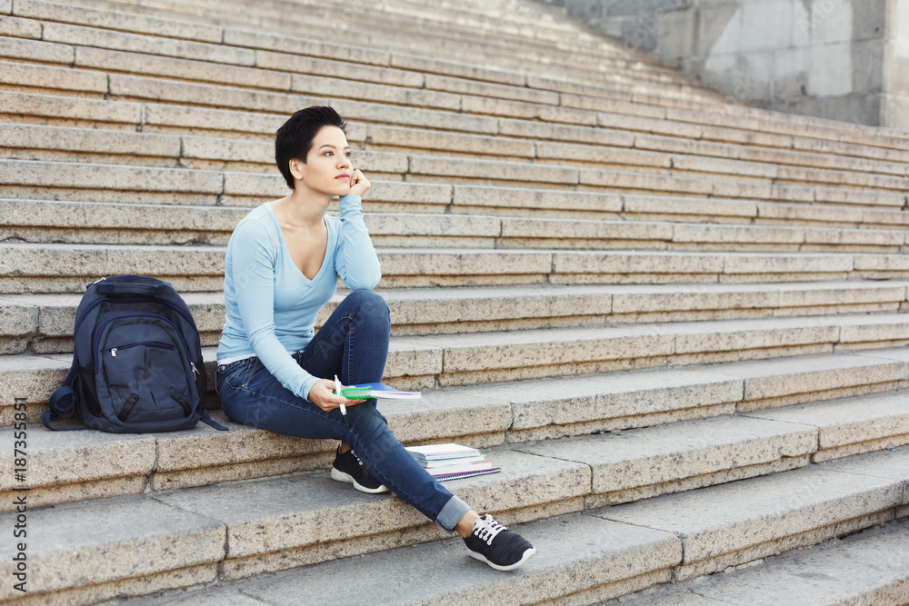 Young thoughtful student girl making notes in notebook