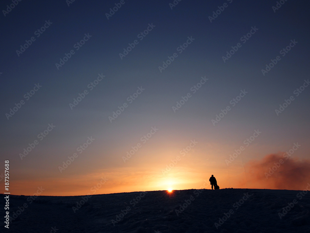 Silhouette of a man standing on snow mountain toward sunset 
