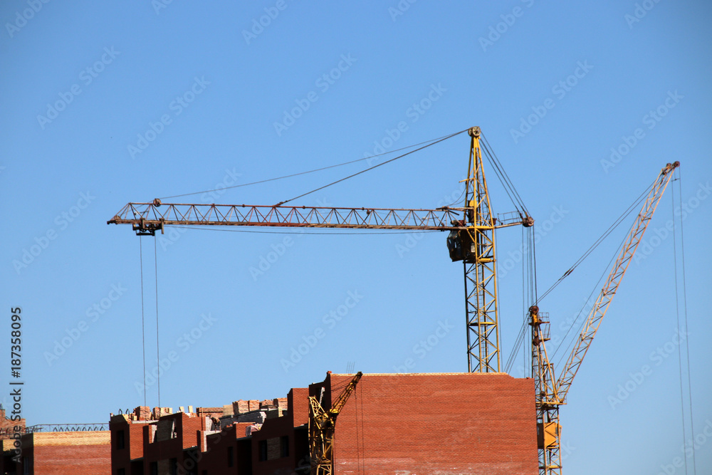 Old tower cranes raise brick blocks against a blue sky