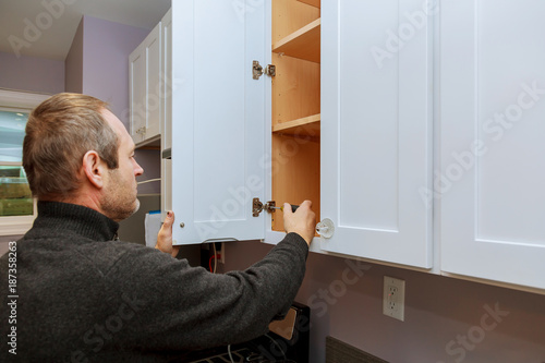 Worker sets a new handle on the white cabinet with a screwdriver installing kitchen cabinets