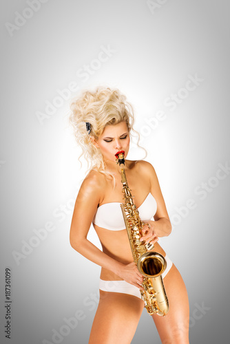 Photography Playing jazz / Beautiful pinup model playing saxophone on grey background
