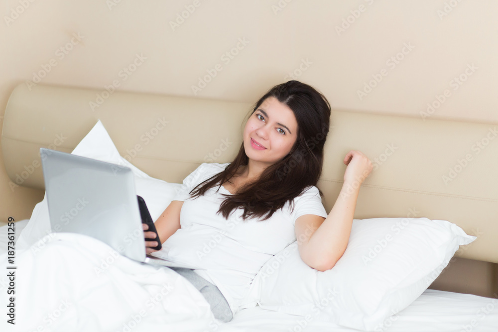 Happy young beautiful woman working on a laptop sitting on the bed at home Happy young beautiful woman working on a laptop sitting on the bed at home