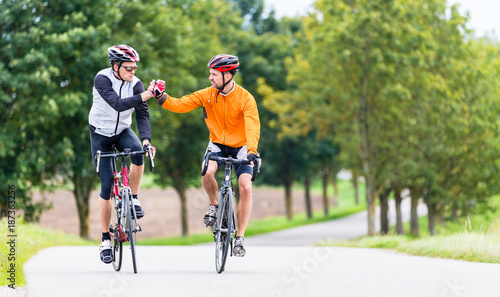 Racing cyclists after sport and fitness workout giving high five in finish