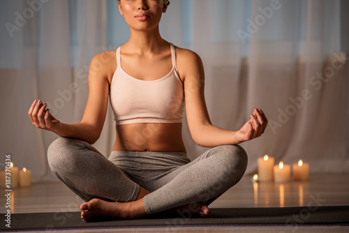 Calm young woman is meditating in peaceful atmosphere. She is sitting in lotus position on mat