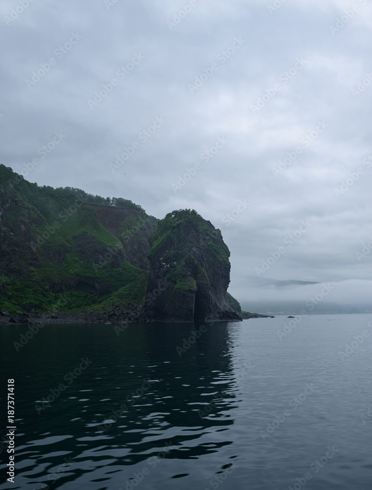 Rocky cliffs of the coastline of Shiretoko National Park hidden in a heavy layer of fog, Shiretoko National Park, Hokkkaido, Japan
