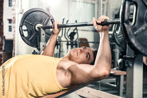 Man lies on the gym bench and prepares for barbell exercises
