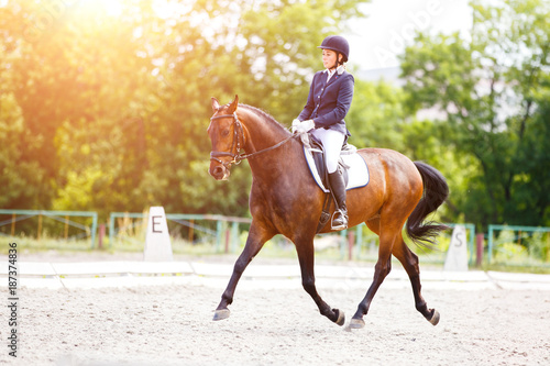 Young rider woman on her bay horse on advanced test dressage competition at sunny day © skumer