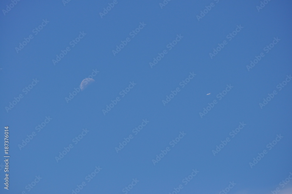 Moon and Distant Airplane with Blue Sky Background