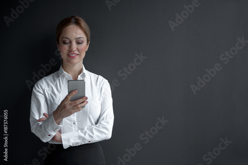 Portrait of smiling businesswoman typing in phone. Labor and technology concept. Copy space