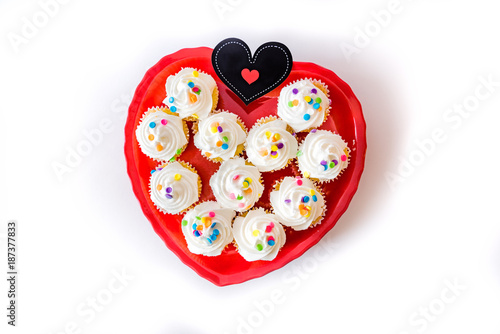 Heart shaped red dish full of frosted white cupcakes and black card