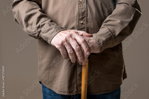 Arms of old man on waking stick. Isolated on grey background. Close up