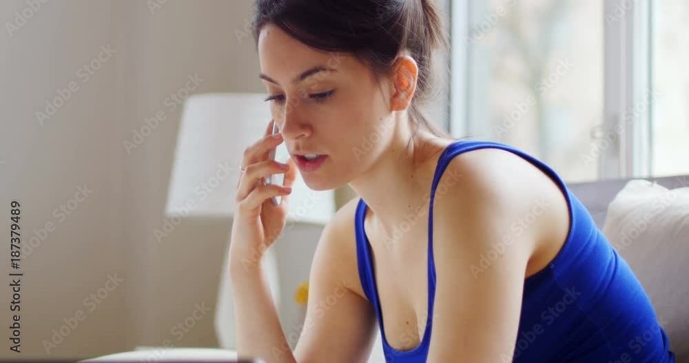Young woman talking on mobile phone while using laptop Young woman talking on mobile phone while using laptop