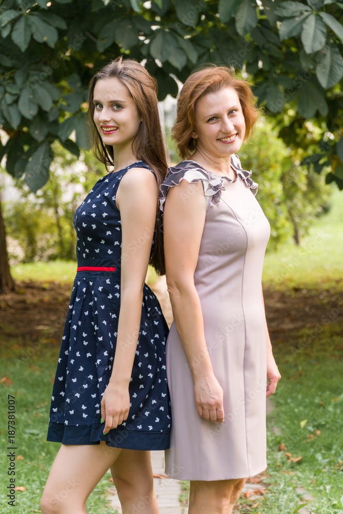 Fototapeta premium Closeup Portrait of Adult Daughter and Mother Outdoors. Pretty Brunette and Her Mom are Looking at the Camera in the Park in Summer.