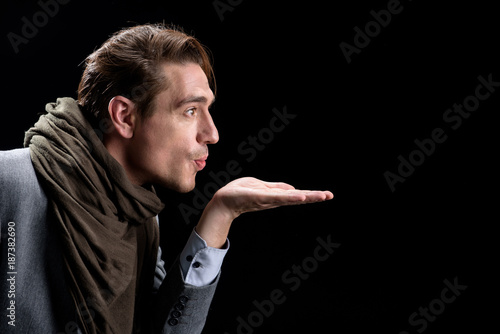 Air-kiss. Side view profile of elegant trendy young positive man is standing and holding palm up while sharing an air kiss. Isolated background and copy space in the right side